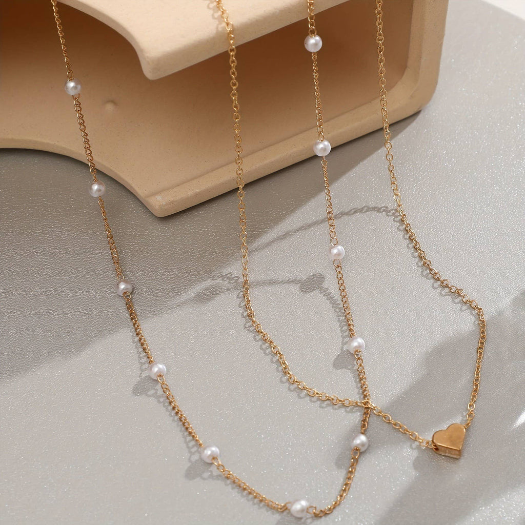 Gold chain necklace with heart charm and pearls on a light gray surface