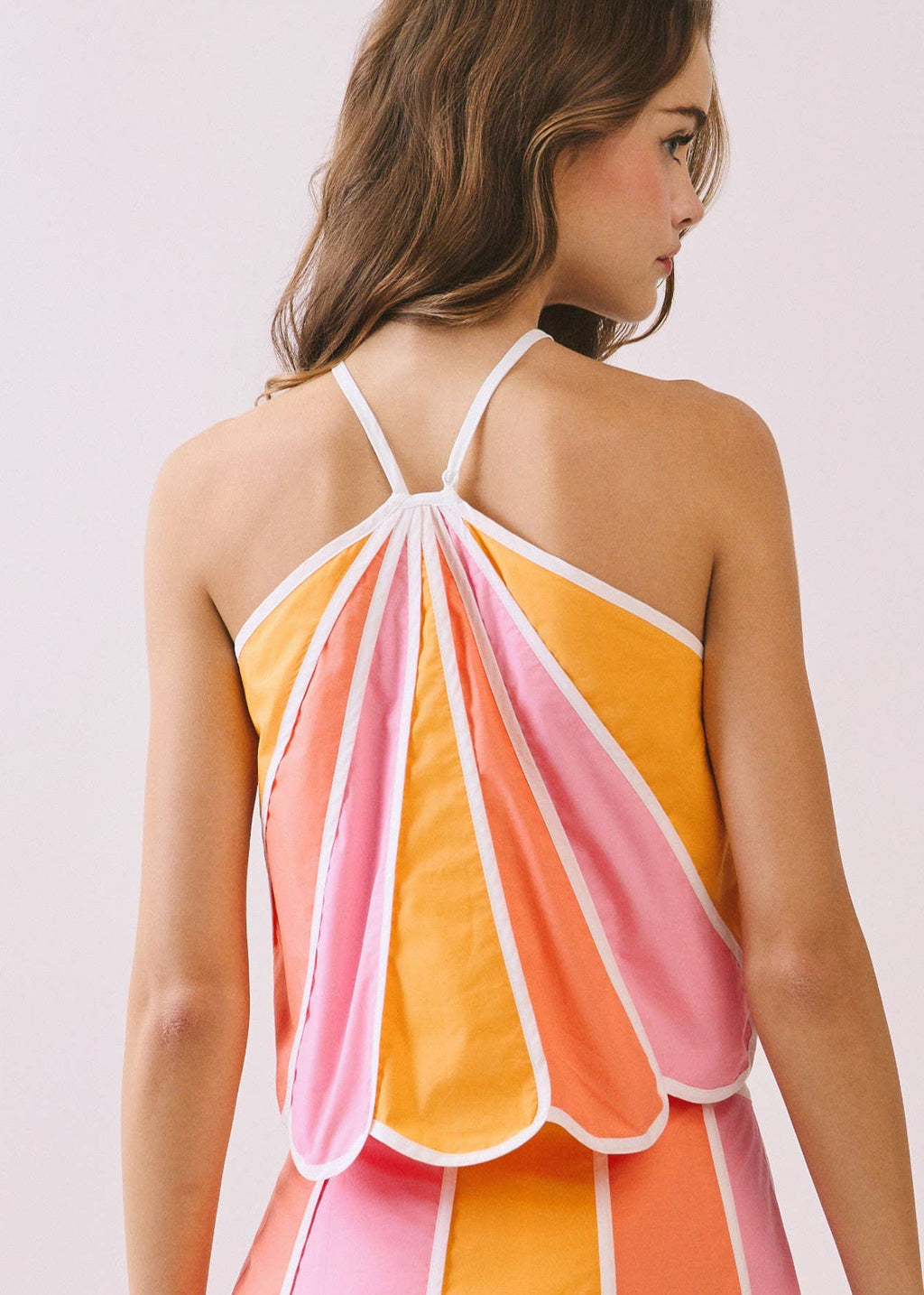 Woman wearing a colorful dress with pink, orange, and yellow stripes on a light background