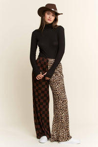 Woman wearing a black turtleneck, checkered pants, and leopard print pants with a brown hat on a beige background.