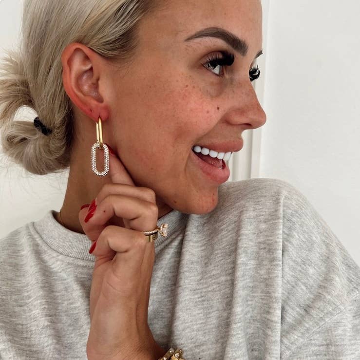 Woman wearing gold earrings and a ring, smiling.