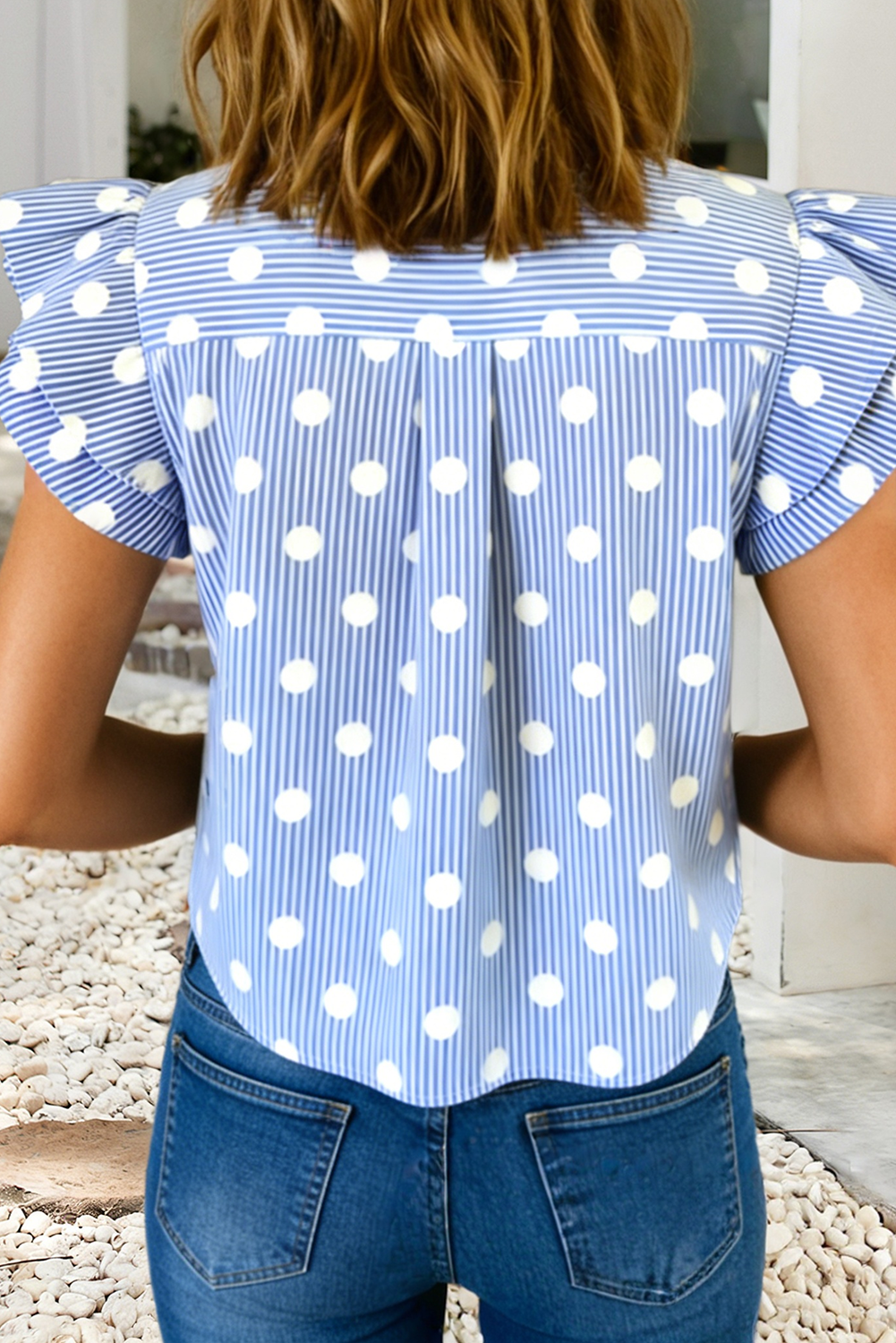 Woman wearing a blue and white polka dot blouse with ruffled sleeves.
