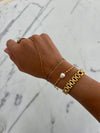 Hand wearing multiple gold bracelets on a marble surface