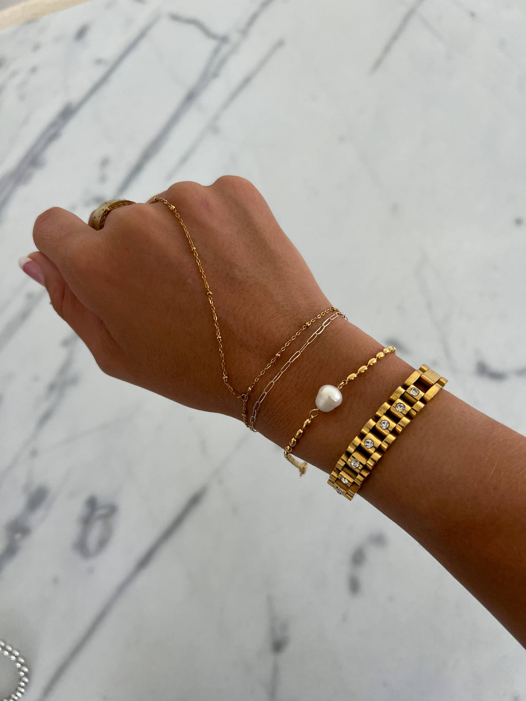 Hand wearing multiple gold bracelets on a marble surface