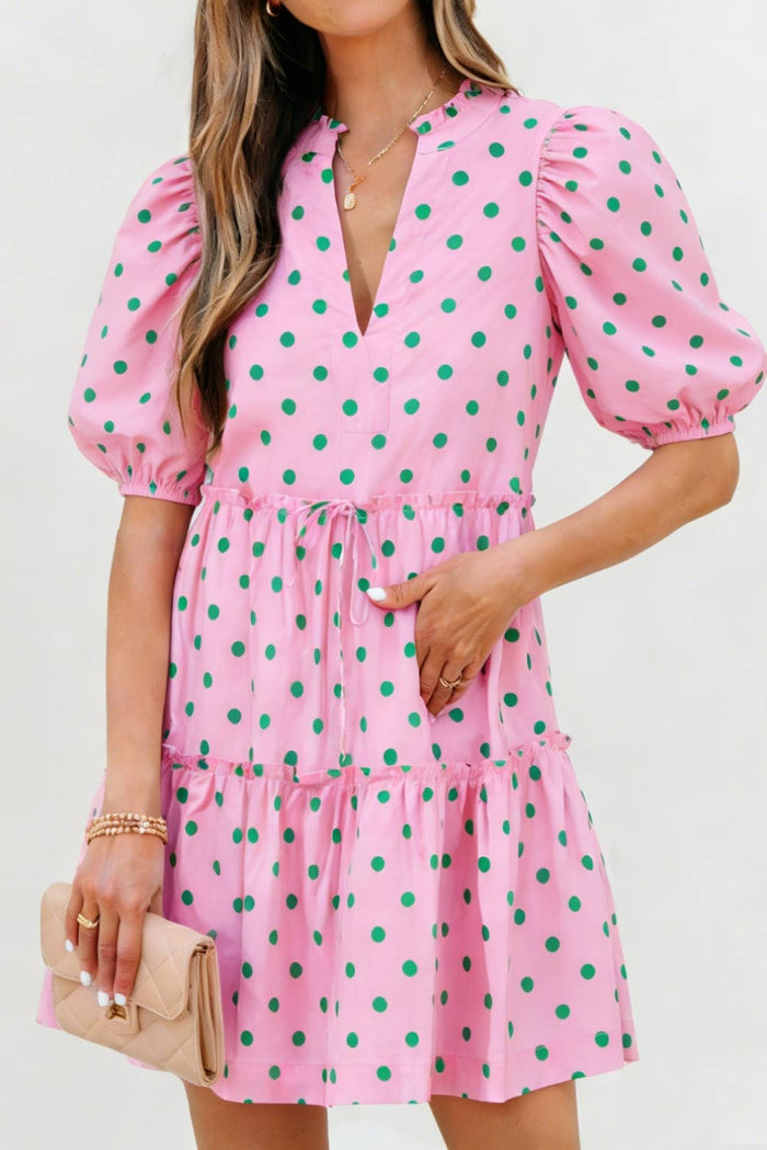 Woman wearing a pink polka dot dress with green dots against a white background