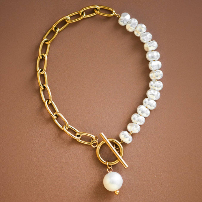 Gold chain bracelet with white pearls on a brown background