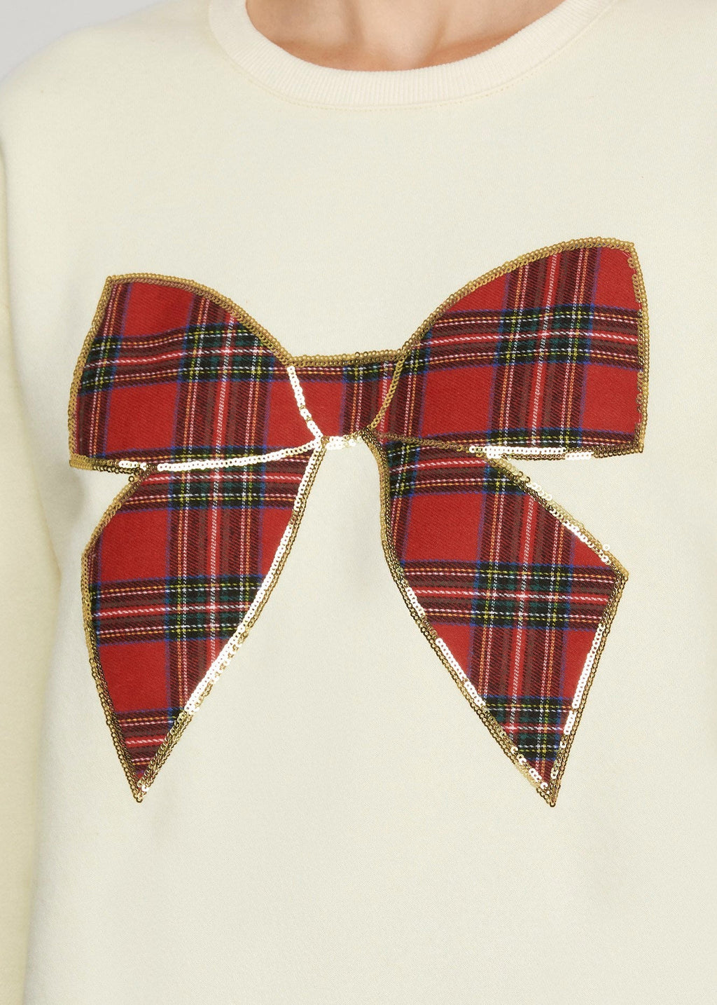 Woman sitting on a box with gift boxes around her, wearing a cream sweater with a red tartan bow design.