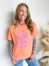 Woman wearing an orange t-shirt with pink text, standing against a neutral background