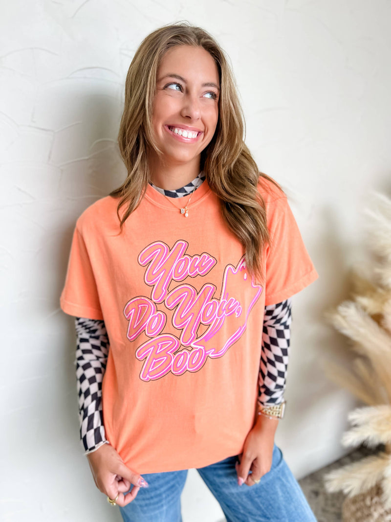 Woman wearing an orange t-shirt with pink text, standing against a neutral background