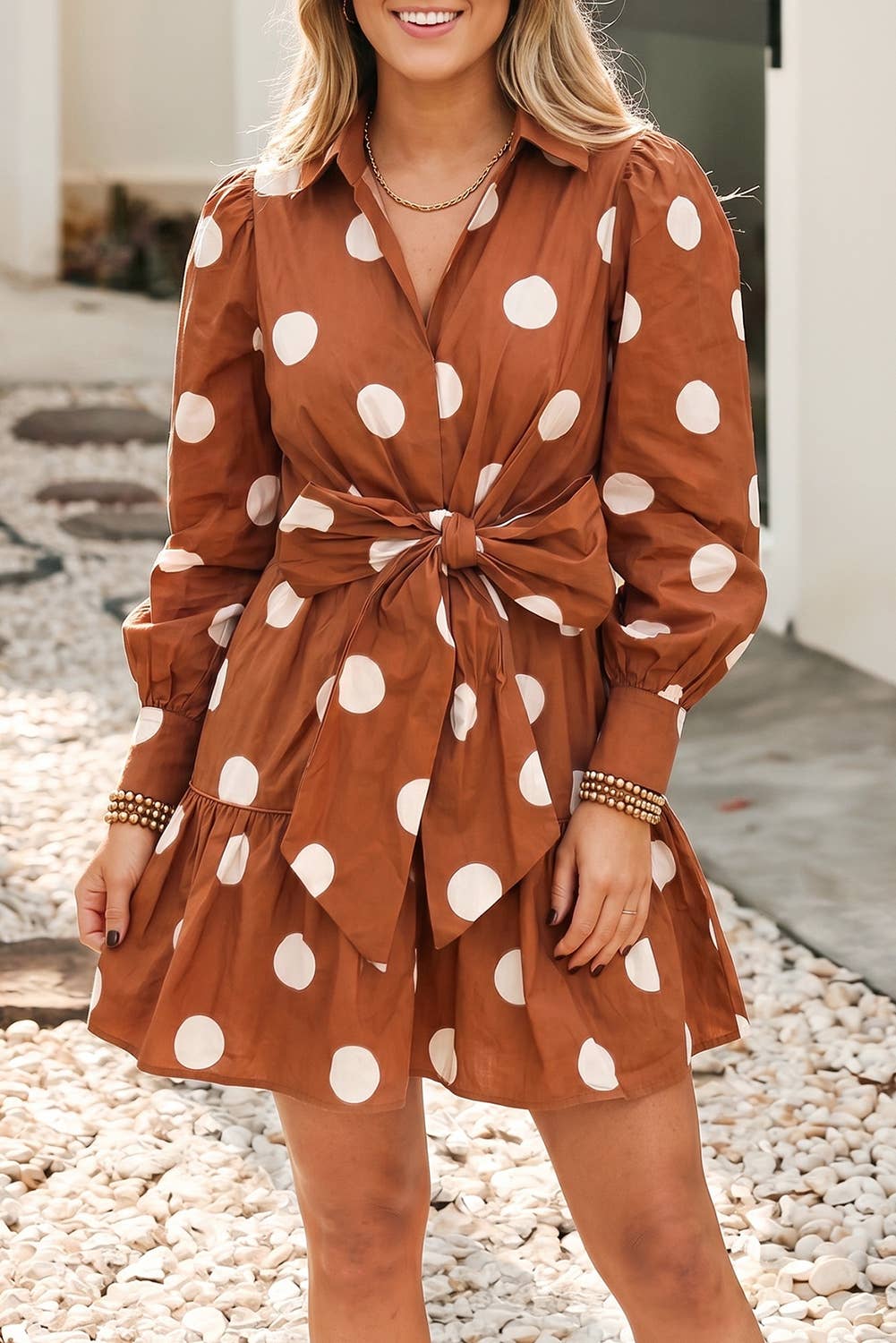 Woman wearing a brown dress with white polka dots standing on pebbles.