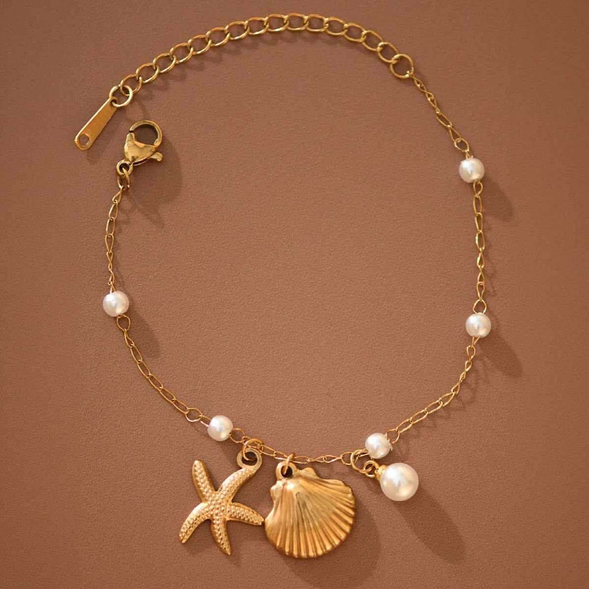 Gold bracelet with starfish, shell, and pearl charms on a brown background