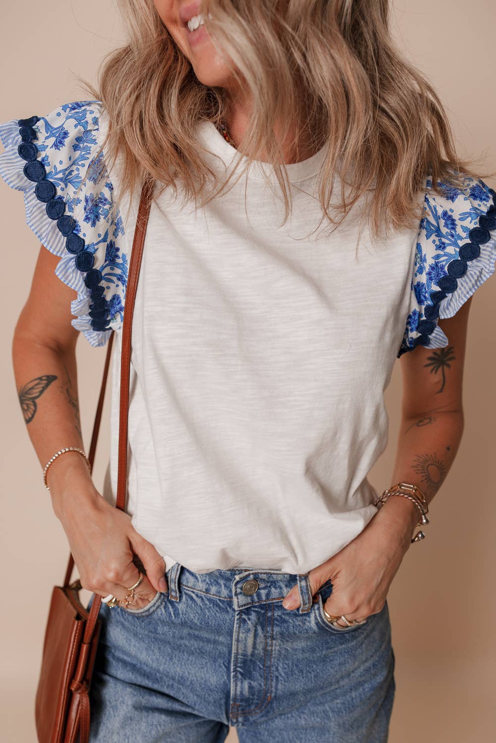 Woman wearing a white t-shirt with blue floral sleeves against a beige background