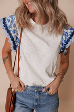 Woman wearing a white t-shirt with blue floral sleeves against a beige background