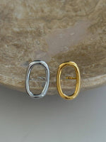 Silver and gold oval-shaped earrings on a stone surface