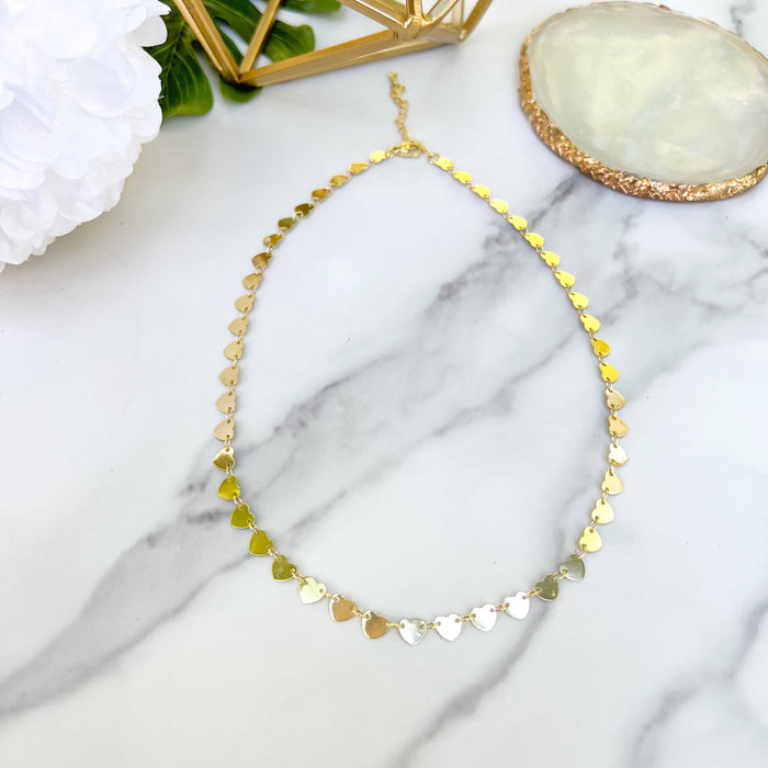 Gold heart-shaped necklace on a marble surface with decorative elements.
