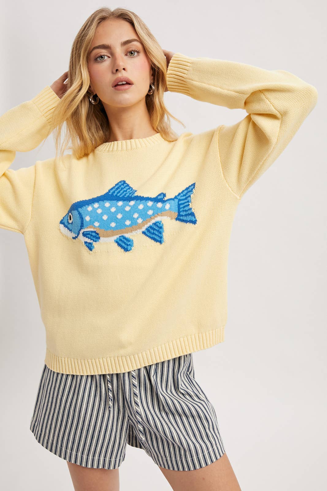 Woman wearing a yellow sweater with a blue fish design on a white background