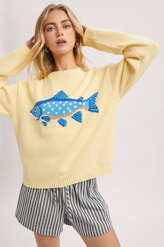 Woman wearing a yellow sweater with a blue fish design on a white background