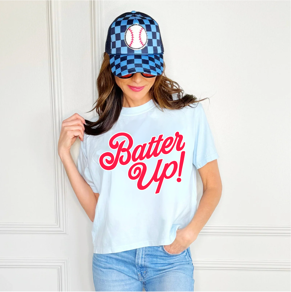 Woman wearing a light blue t-shirt with 'Batter Up!' text and striped pants in a room.