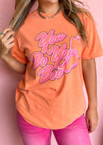 Person wearing an orange t-shirt with pink text and pink pants against a pink background