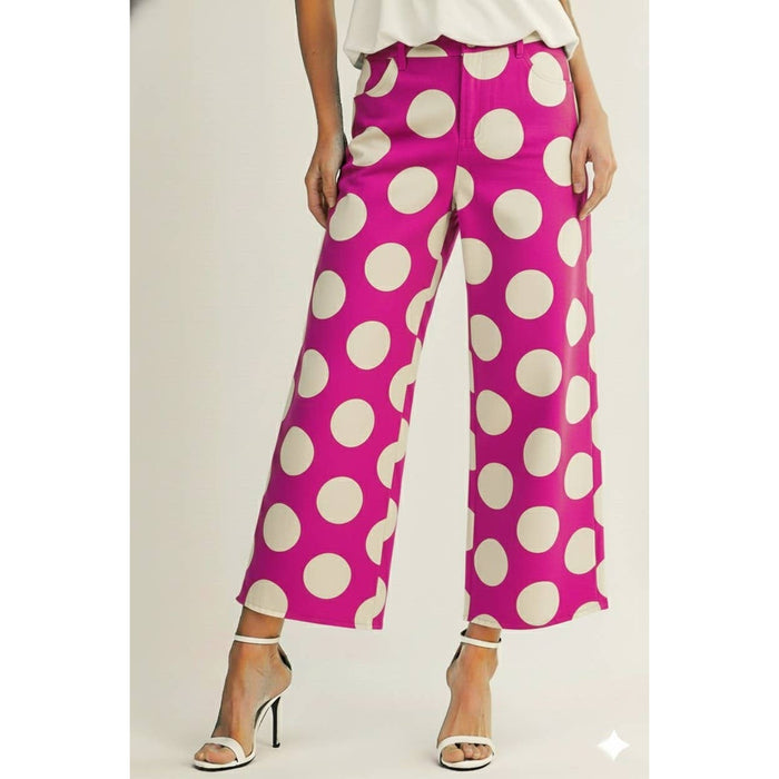 Pink pants with white polka dots worn by a person on a plain background