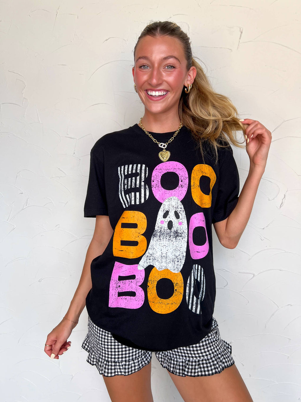 Person wearing a black t-shirt with colorful text design against a white wall.