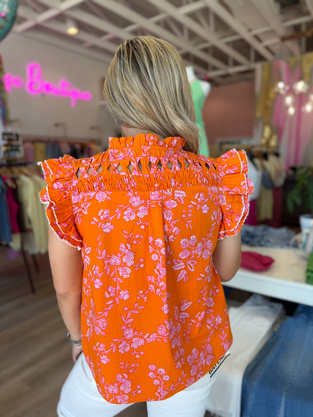 Woman wearing an orange floral blouse and white pants in a clothing store.