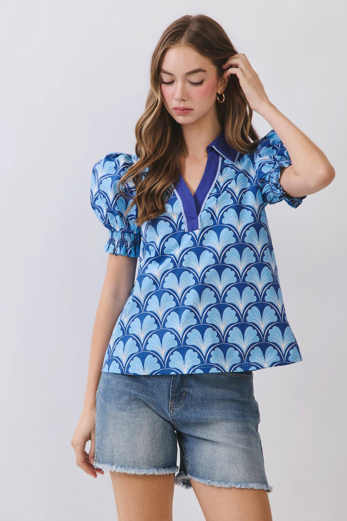 Woman wearing a blue patterned top and denim shorts on a light gray background