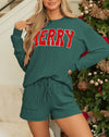 Woman wearing a green outfit with 'MERRY' text in red, standing in front of a decorated Christmas tree.