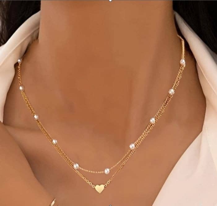 Gold necklace with heart pendant on a person wearing a beige top.
