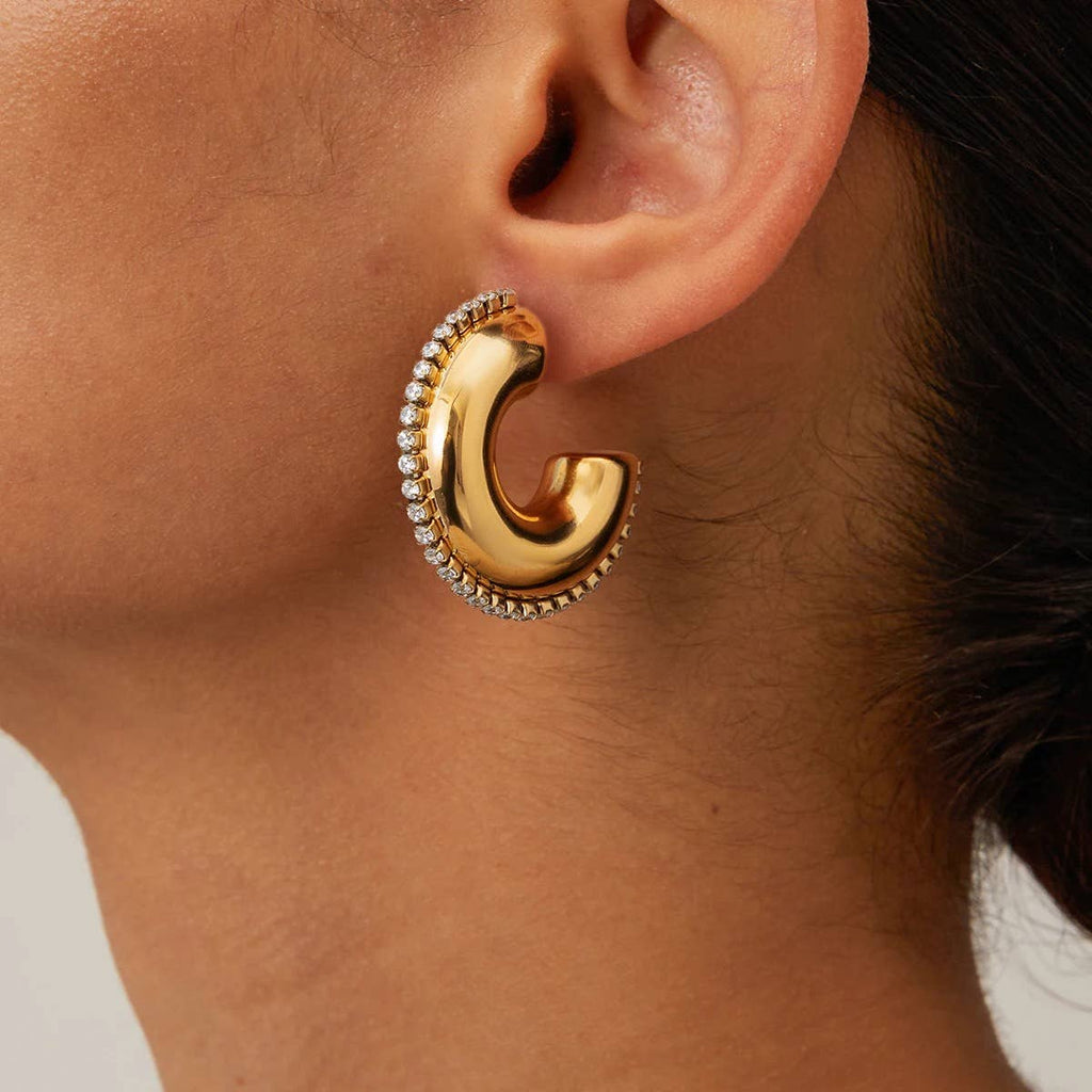 Gold hoop earring with embedded stones worn by a person.
