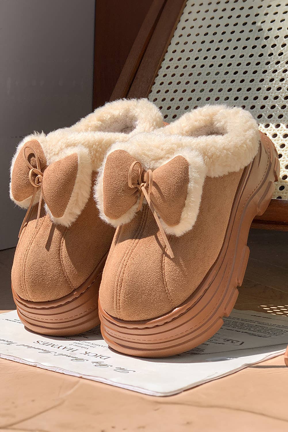 Pair of tan slip-on shoes with fluffy white trim on a newspaper surface.