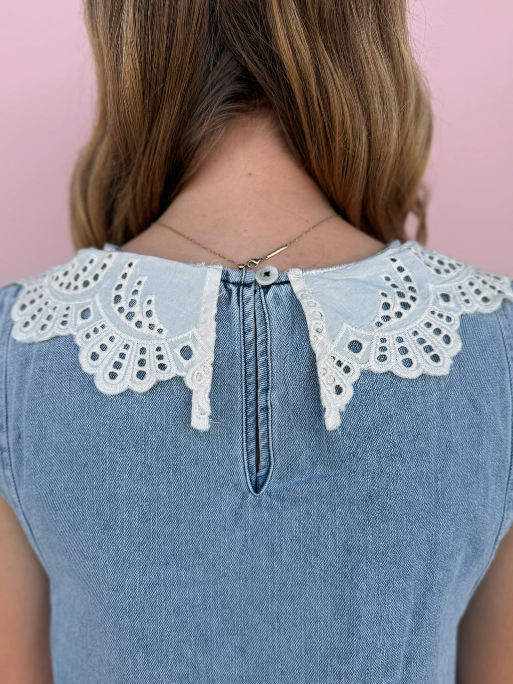 Blue denim dress with white lace collar against a pink background