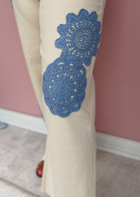 Beige pants with blue lace detailing on a pink wall background