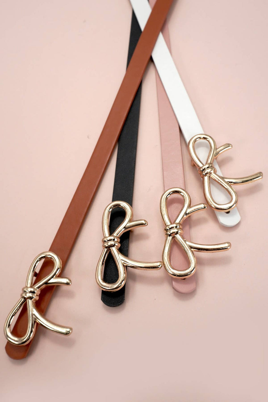 Bow-shaped belt buckles in gold, black, and white on a pink background