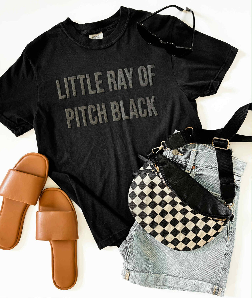 Black t-shirt with 'Little Ray of Pitch Black' text, checkered bag, denim shorts, and brown sandals on a white background