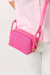 Pink woven handbag with gold accents held by a person wearing a pink shirt and white pants.
