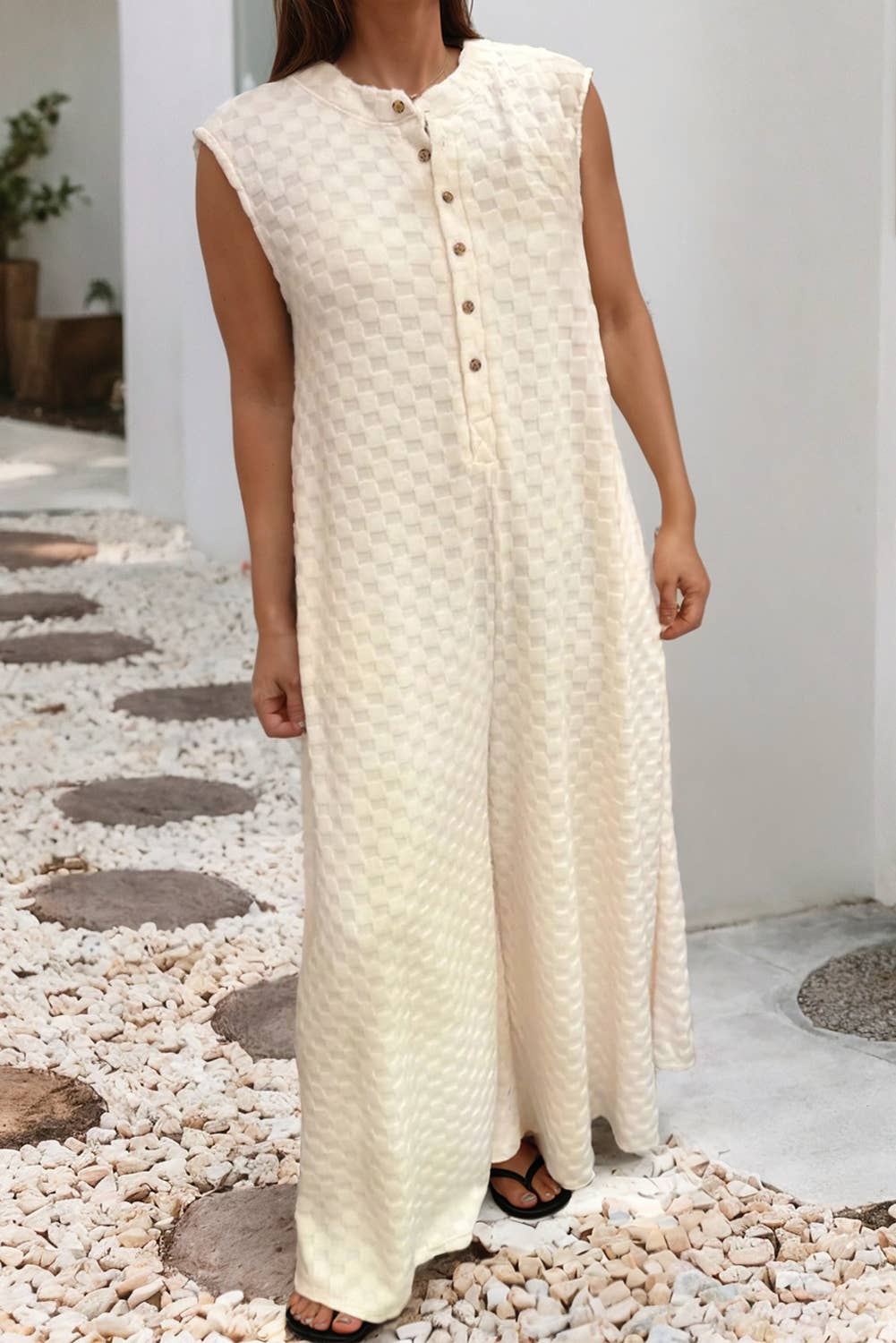 Woman wearing a long, light-colored dress with buttons standing on pebbles.