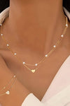 Gold necklaces with heart pendants on a person wearing a light-colored top.