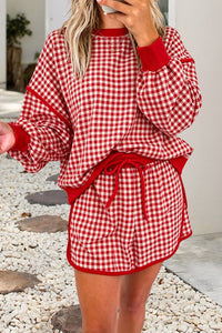 A woman wearing a red and white gingham matching lounge set with long sleeves, a drawstring waist, and shorts, photographed outdoors on a stone path.