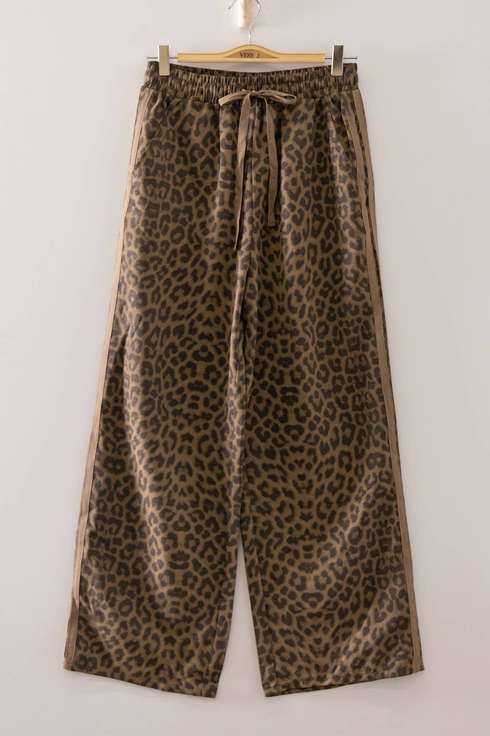 Leopard print pants hanging on a wooden hanger against a white background