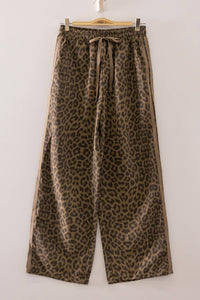 Leopard print pants hanging on a wooden hanger against a white background