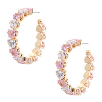 A pair of gold hoop earrings decorated with alternating pink and clear heart-shaped crystals, displayed on a solid white background.
