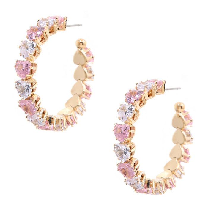 A pair of gold hoop earrings decorated with alternating pink and clear heart-shaped crystals, displayed on a solid white background.