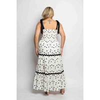 Woman wearing a white dress with black polka dots and a black top, standing against a plain background.
