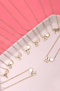Gold necklaces with letter pendants on a pink surface