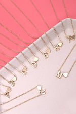 Gold necklaces with letter pendants on a pink surface
