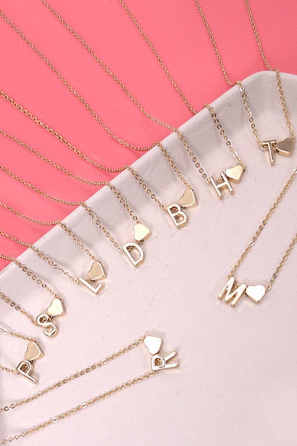 Gold necklaces with letter pendants on a pink surface