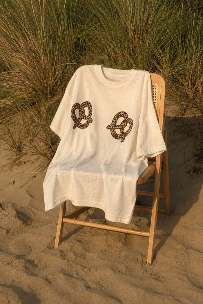 White t-shirt with pretzel design on a wooden chair on a sandy beach.