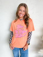 Woman wearing a peach-colored shirt with text and checkered sleeves against a white background