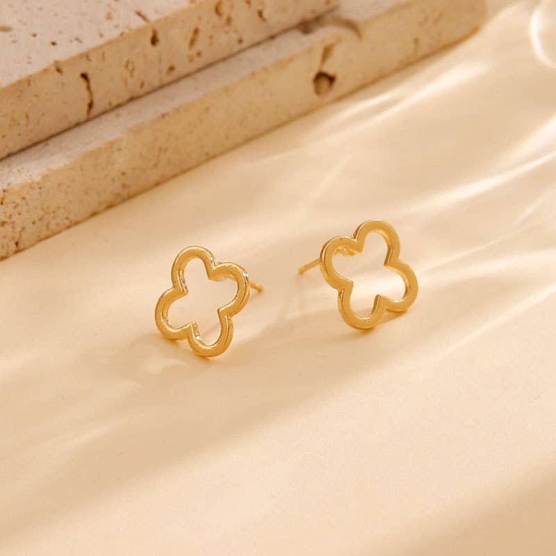 Gold clover-shaped earrings on a beige fabric background