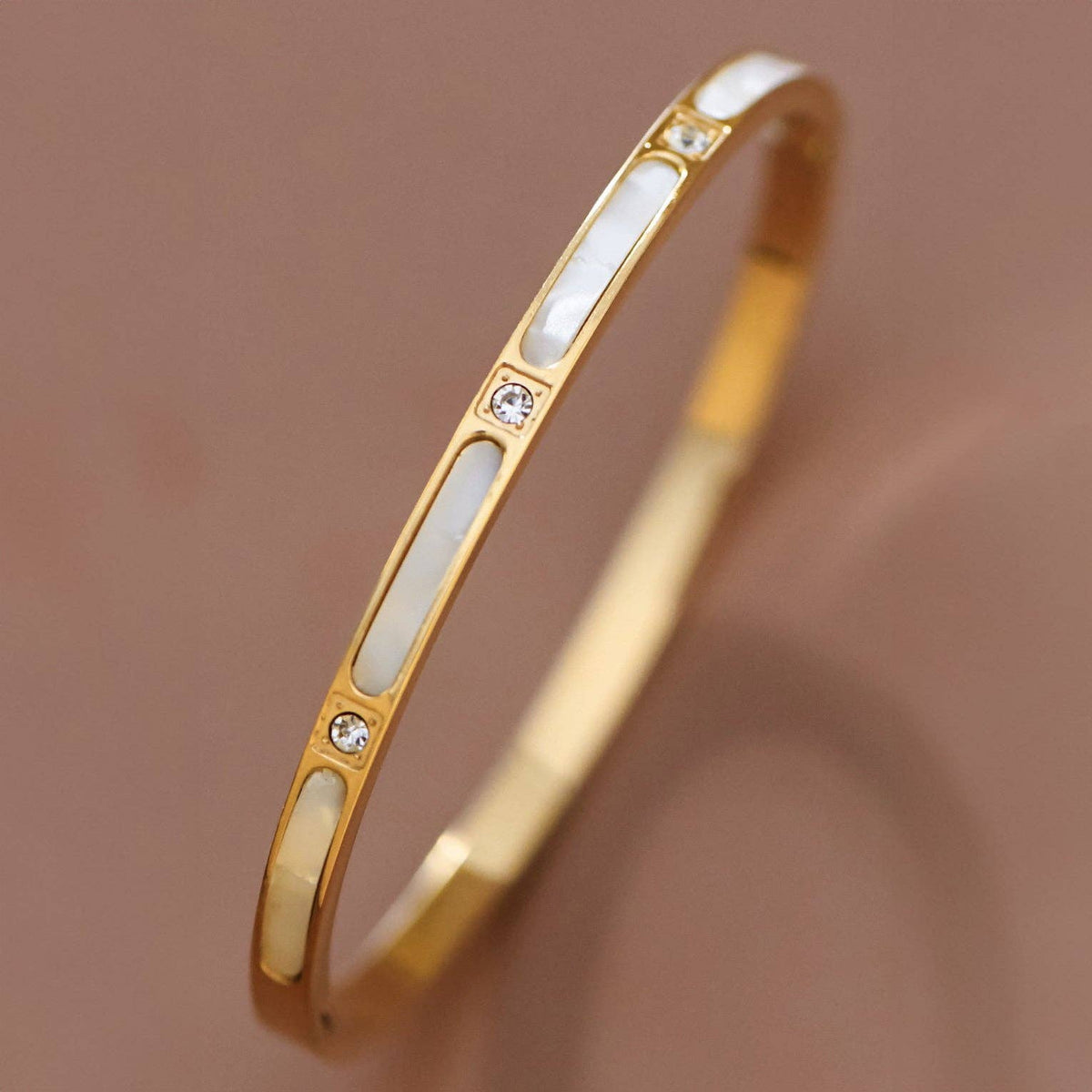 Gold bracelet with white stones on a brown background